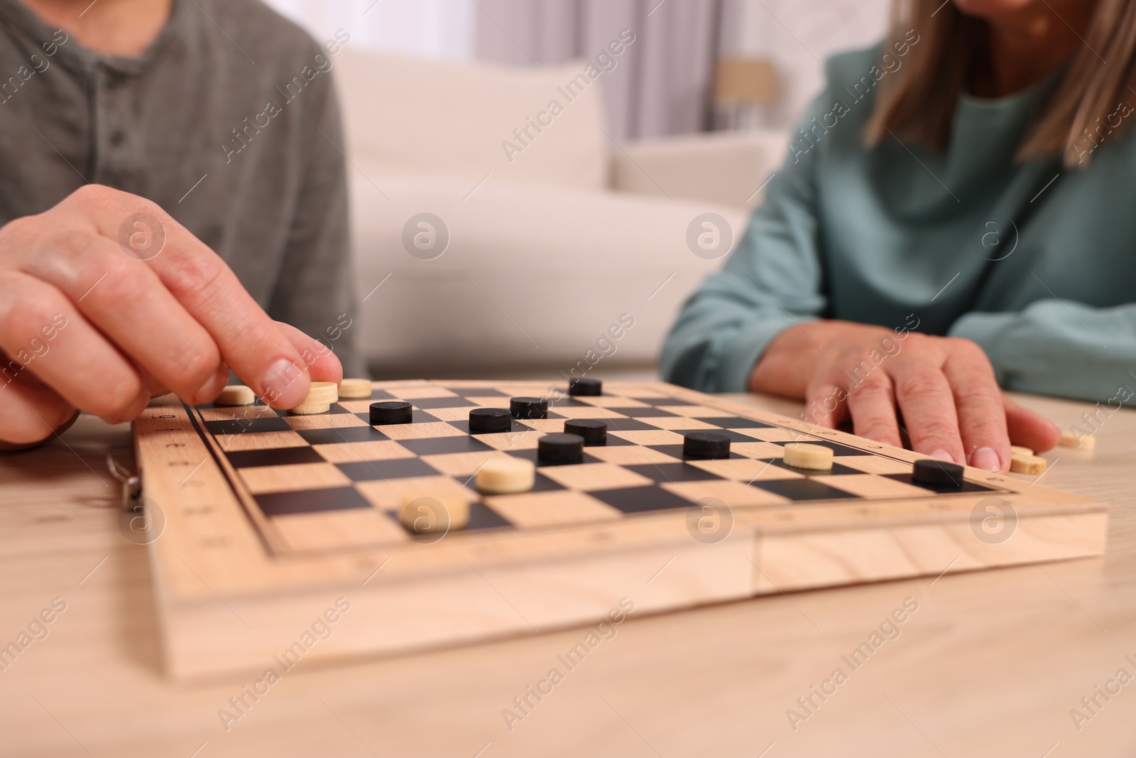 Photo of People playing checkers at wooden table in room, closeup