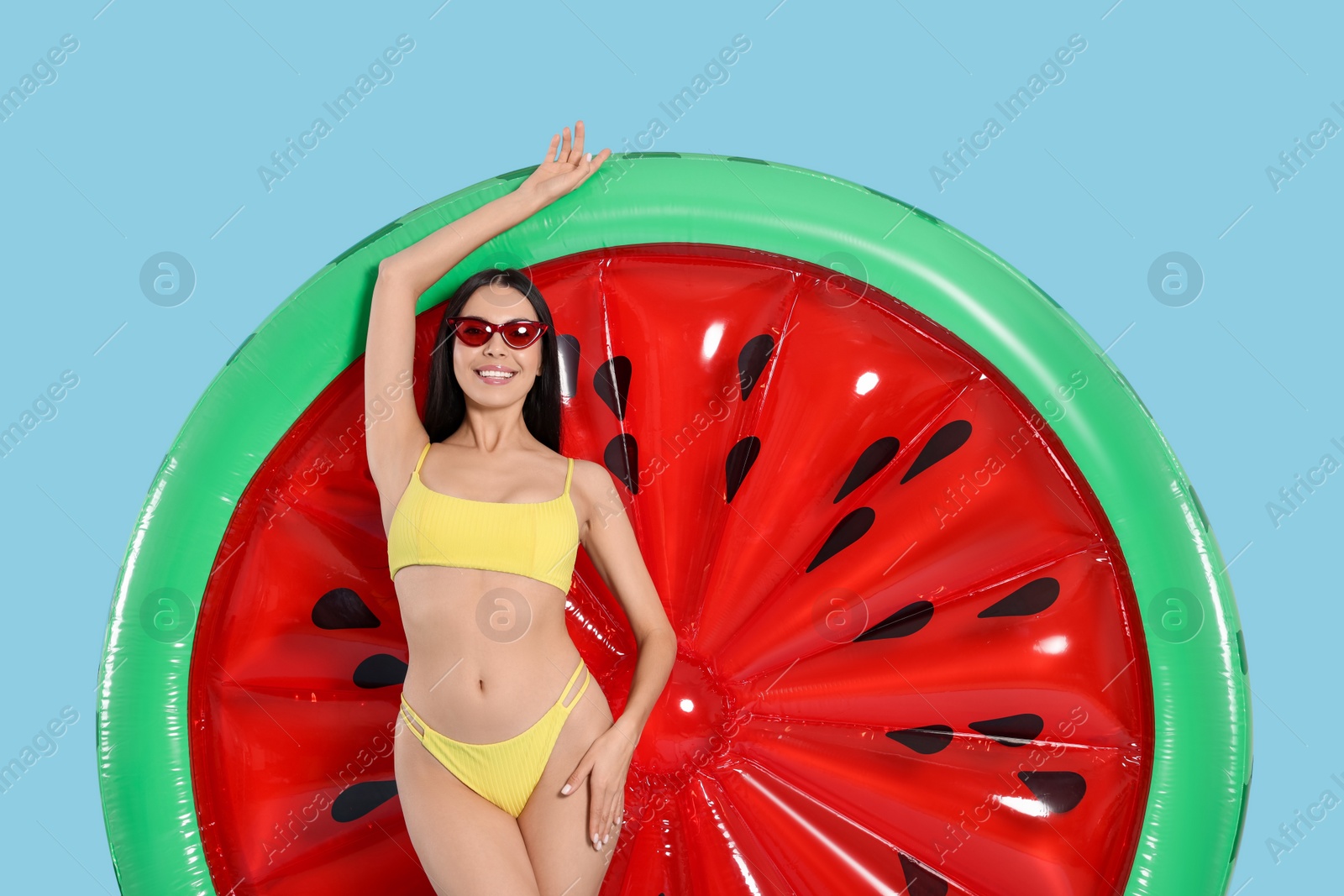 Photo of Young woman in stylish swimsuit near inflatable mattress against light blue background