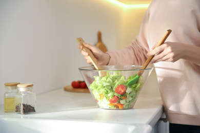 Photo of Young woman cooking salad at counter in kitchen, closeup