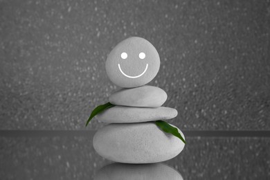 Stack of stones with drawn happy face and green leaves on grey background. Zen concept