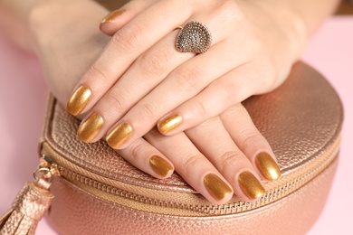 Photo of Woman holding manicured hands with golden nail polish on bag, closeup