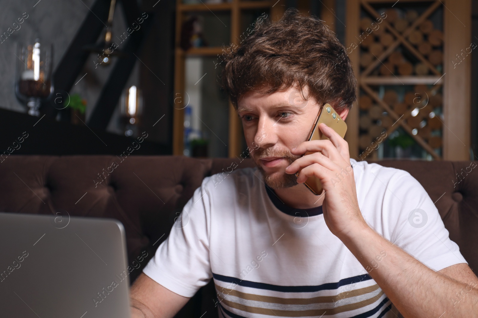 Photo of Handsome man talking on phone while using laptop in cafe