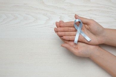 Photo of Woman holding light blue awareness ribbon at white wooden table, top view. Space for text