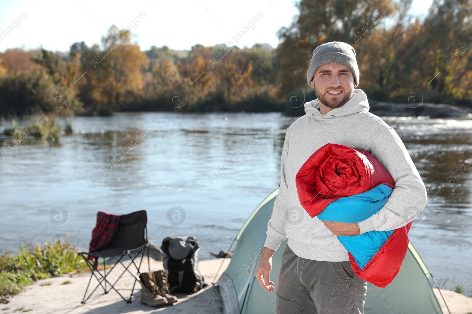 Photo of Young man with sleeping bag near camping tent outdoors. Space for text