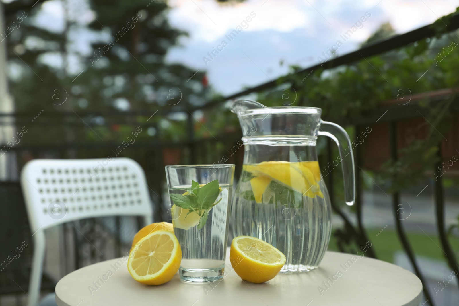 Photo of Jug and glass with refreshing lemon water on light table outdoors