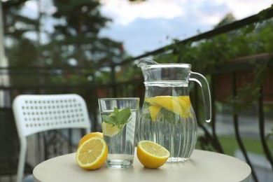 Jug and glass with refreshing lemon water on light table outdoors