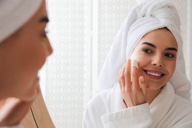 Woman using silkworm cocoon in skin care routine near mirror at home