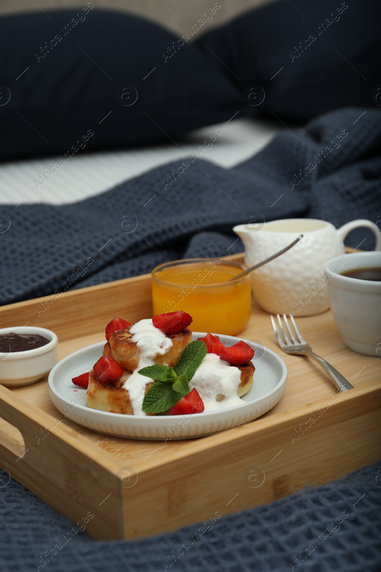 Photo of Cottage cheese pancakes with fresh strawberries, sour cream and mint served for breakfast on wooden tray, closeup