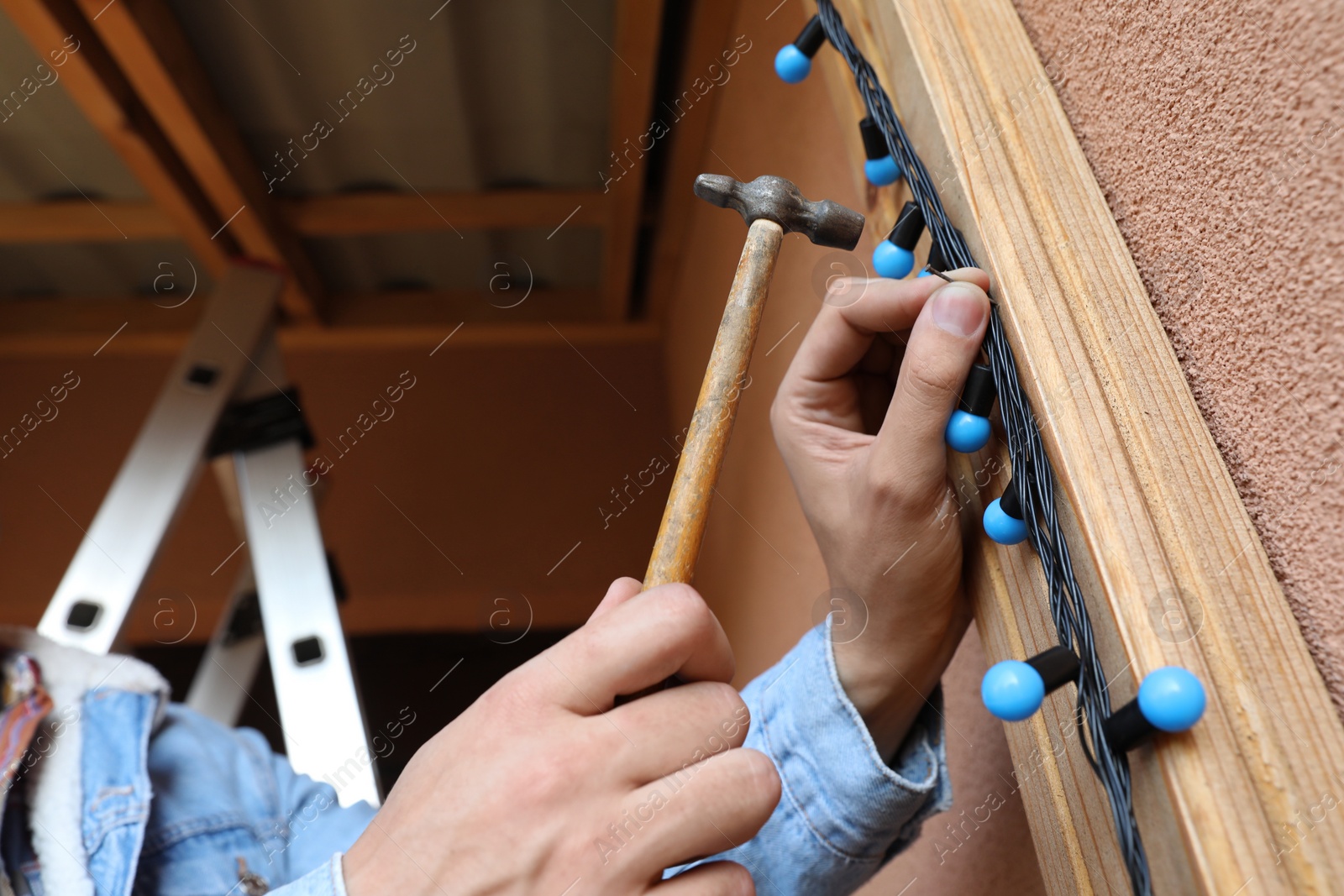 Photo of Man decorating house with Christmas lights outdoors, closeup