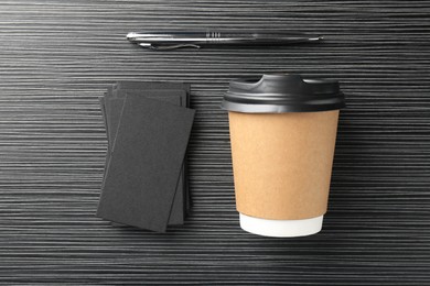 Photo of Blank black business cards, paper cup of coffee and pen on wooden table, flat lay. Mockup for design