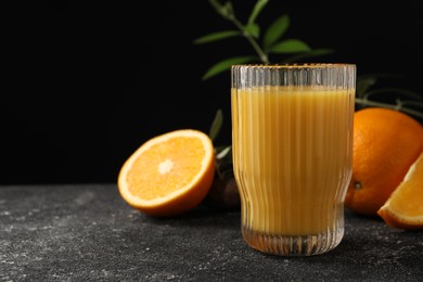Photo of Tasty fresh oranges, juice and leaves on black table, closeup. Space for text