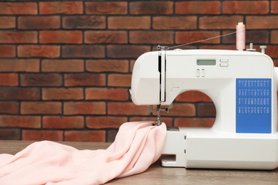 Photo of Sewing machine with fabric on wooden table against brick wall