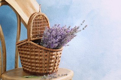 Wicker basket with lavender flowers on chair against color background