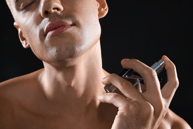 Photo of Young man using perfume on black background, closeup