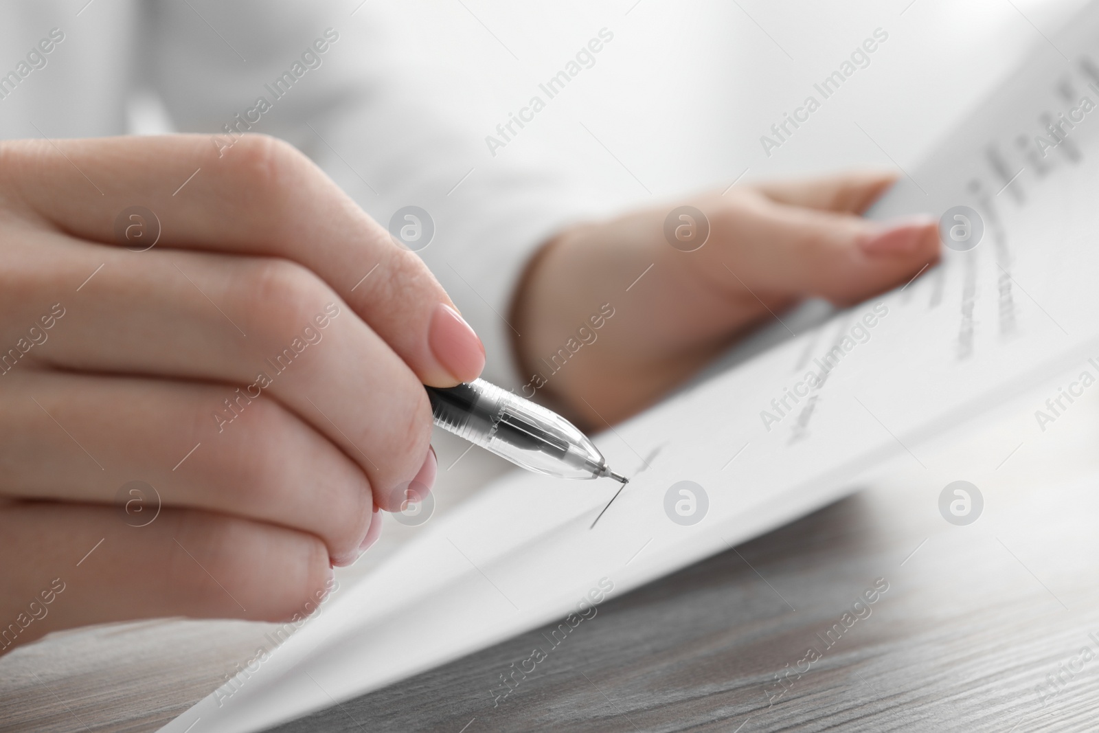 Photo of Woman signing documents at wooden table in office, closeup