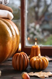 Photo of Beautiful burning candles in shape of pumpkins on wooden table near window. Autumn atmosphere