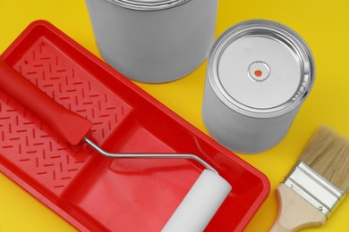 Photo of Cans of orange paint, brush, roller and container on yellow background, above view