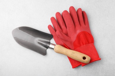 Photo of Pair of red gardening gloves and trowel on light grey table, top view