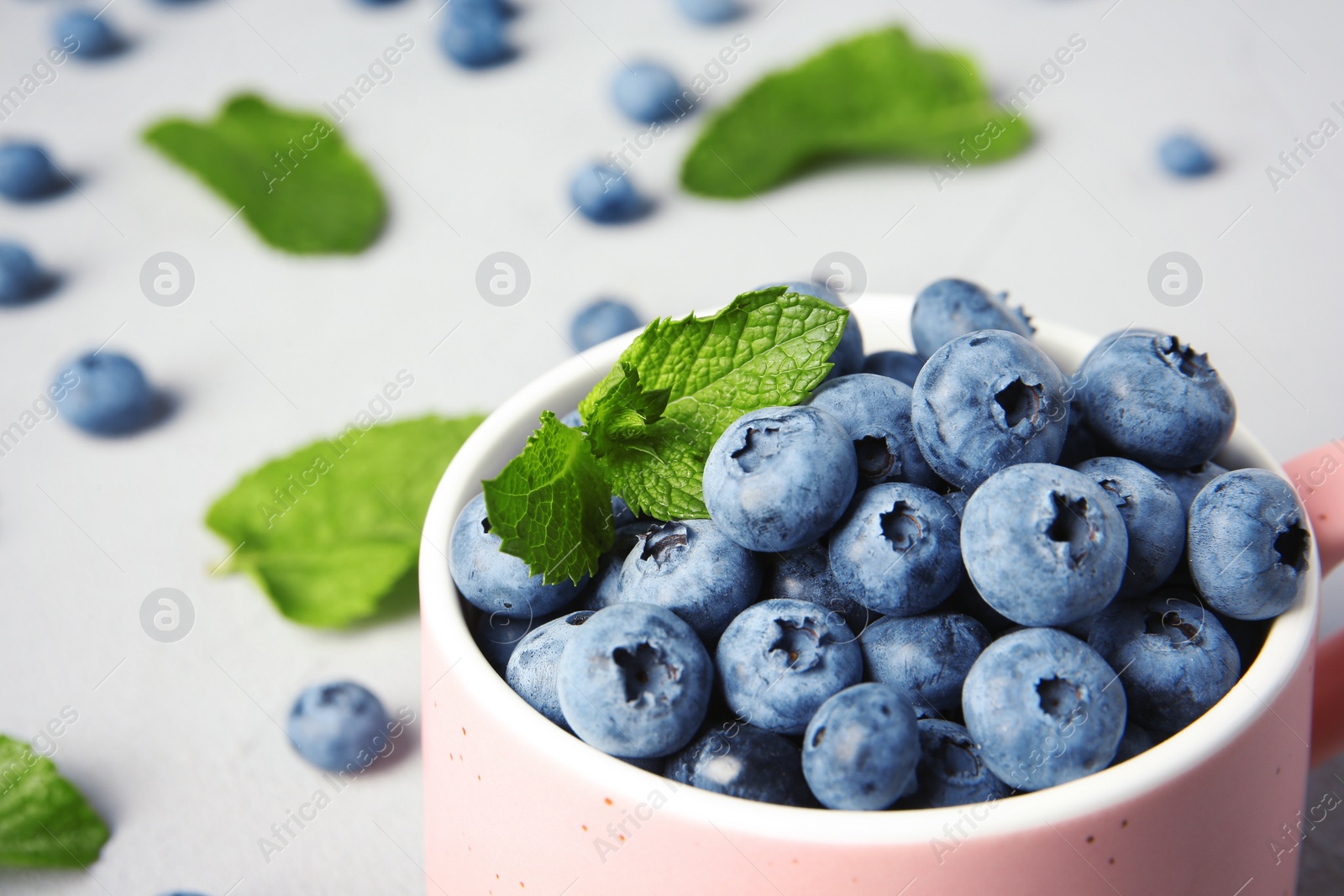 Photo of Cup with juicy blueberries and green leaves on color table