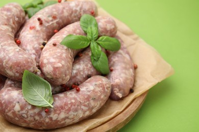 Photo of Board with raw homemade sausages, basil leaves and peppercorns on green table, closeup. Space for text