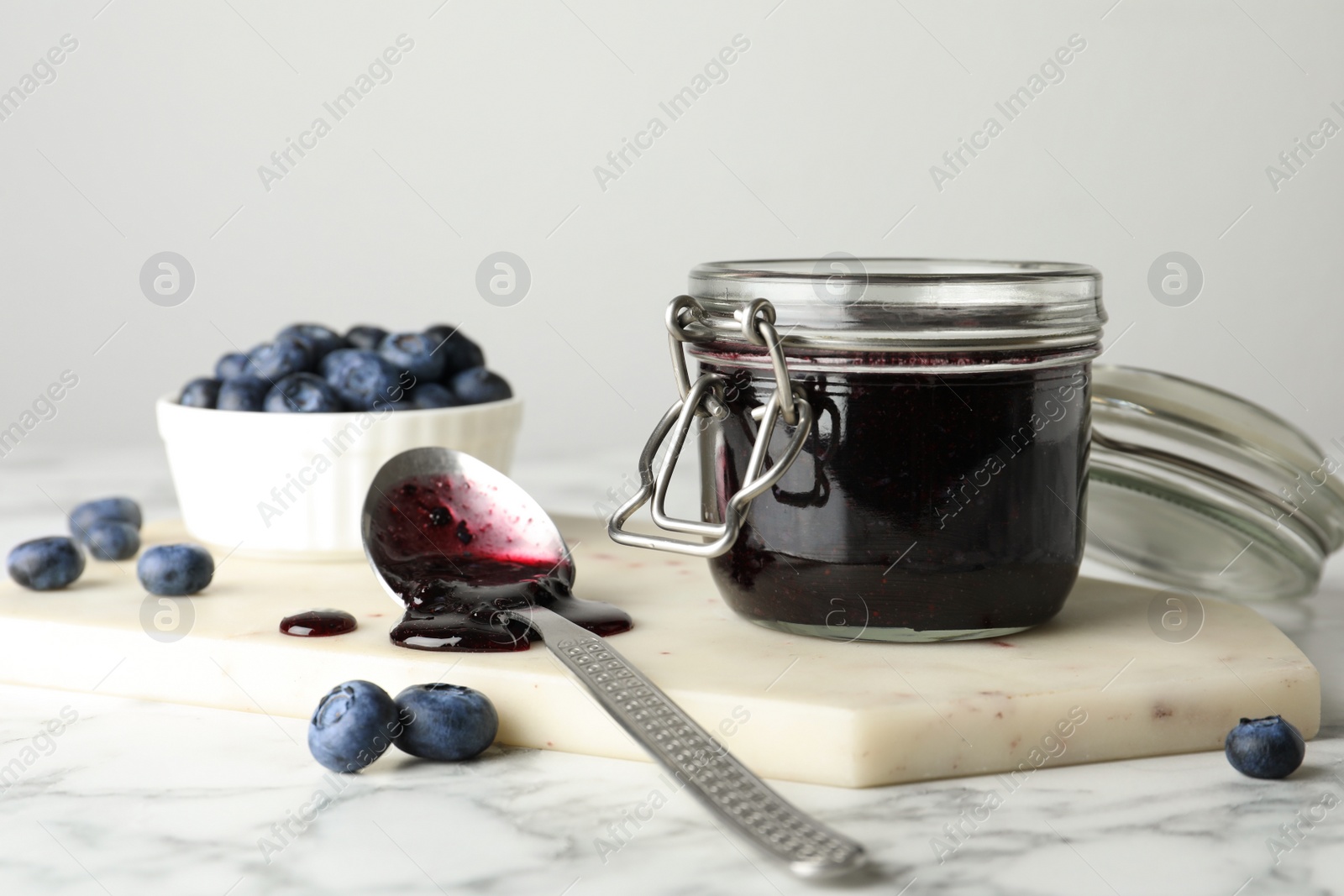 Photo of Jar of blueberry jam and fresh berries on white marble table