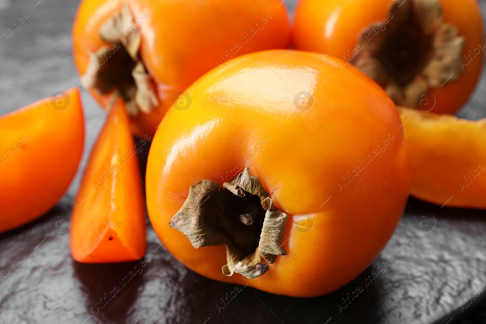 Photo of Delicious ripe persimmons on dark textured table, closeup