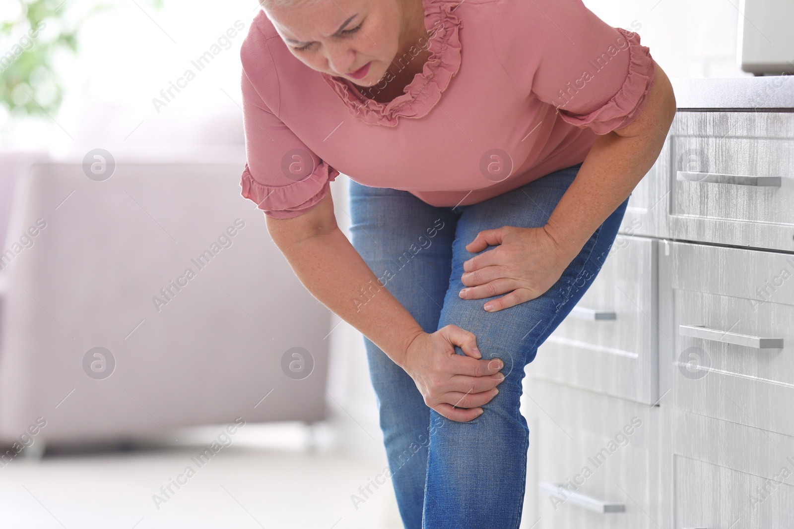 Photo of Senior woman suffering from knee pain in kitchen