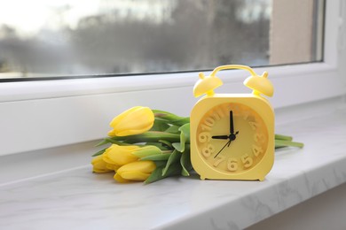 Photo of Yellow alarm clock and wonderful tulips on window sill indoors. Spring atmosphere