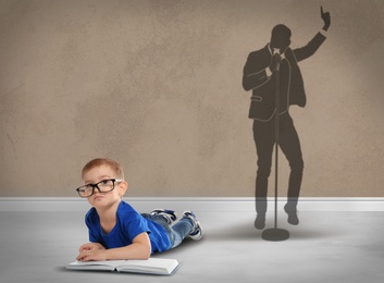 Image of Little boy with book dreaming to be singer. Silhouette of man behind kid's back