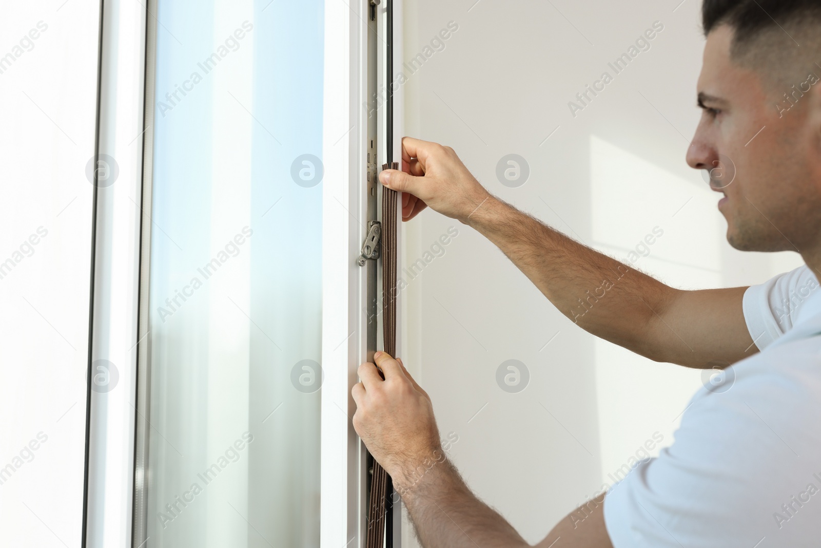 Photo of Man putting rubber draught strip onto window indoors, focus on hands