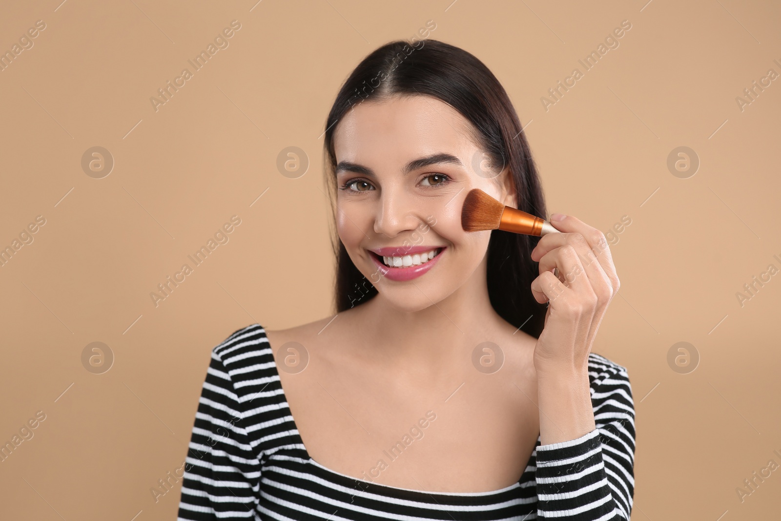 Photo of Beautiful woman applying makeup on light brown background