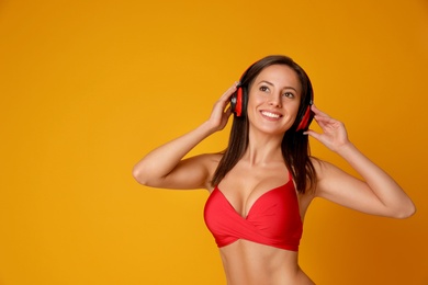 Photo of Pretty sexy woman with slim body in stylish red bikini and headphones on orange background, space for text