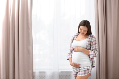 Young beautiful pregnant woman near window at home