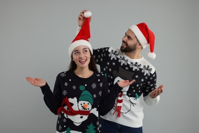Photo of Happy young couple in Christmas sweaters and Santa hats on grey background
