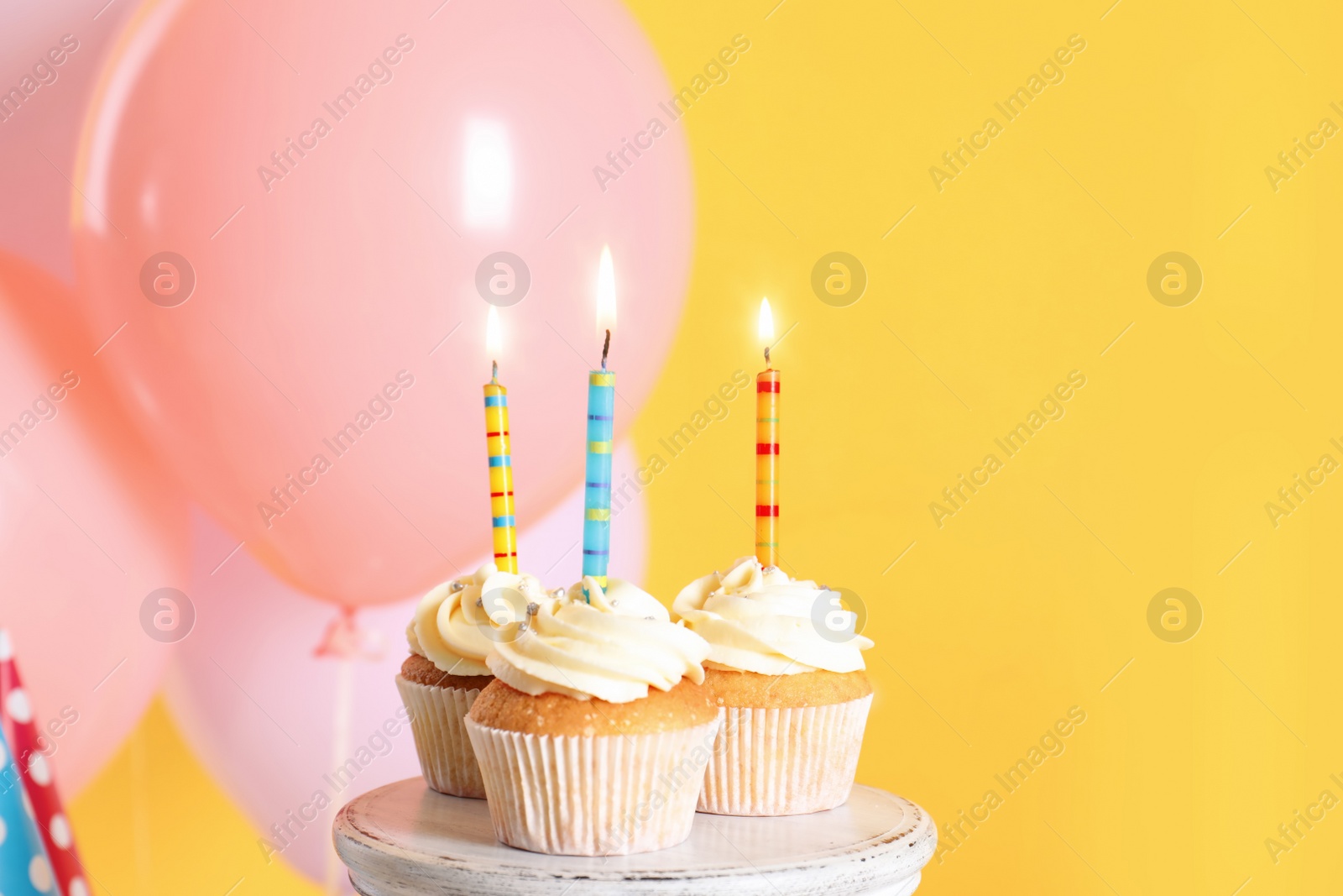 Photo of Stand with birthday cupcakes and party balloons on color background. Space for text