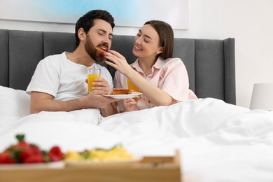Photo of Tasty breakfast. Happy wife feeding her husband in bed at home
