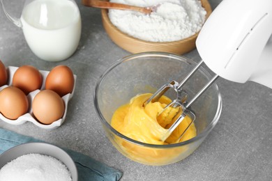 Photo of Beating eggs in glass bowl with mixer on light grey table