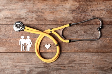 Flat lay composition with heart, stethoscope and paper silhouette of family on wooden background. Life insurance concept