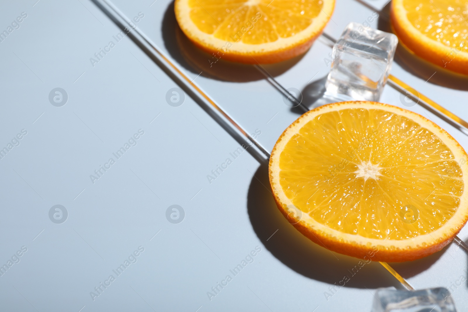 Photo of Slices of juicy orange and ice cubes on light blue background, closeup. Space for text