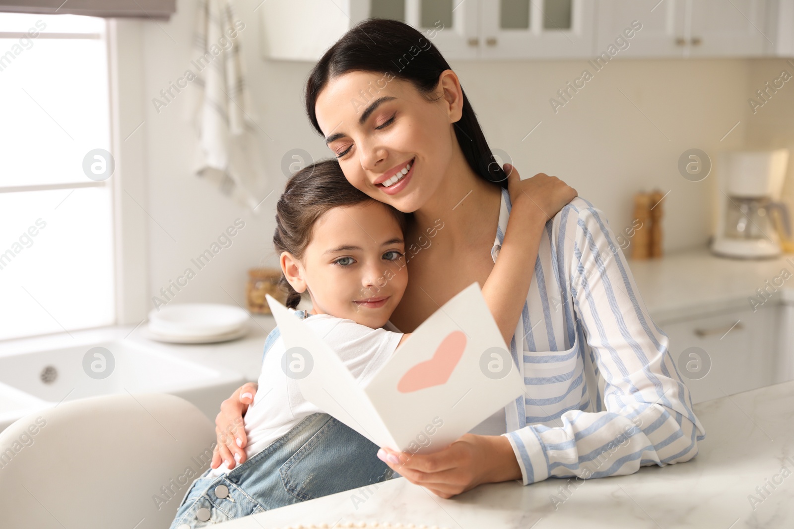 Photo of Little daughter congratulating her mom at table in kitchen. Happy Mother's Day