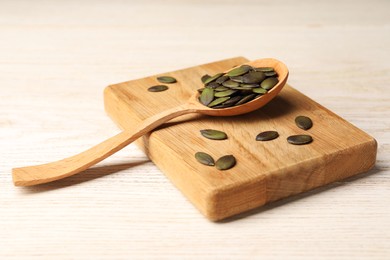 Spoon with pumpkin seeds on wooden table, closeup
