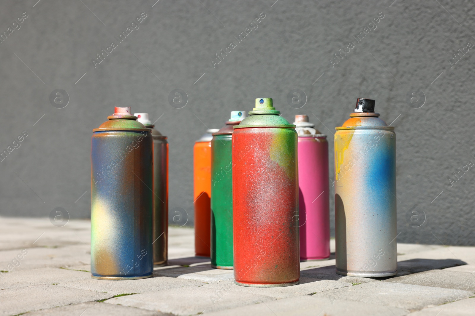 Photo of Cans of different spray paints on pavement near wall