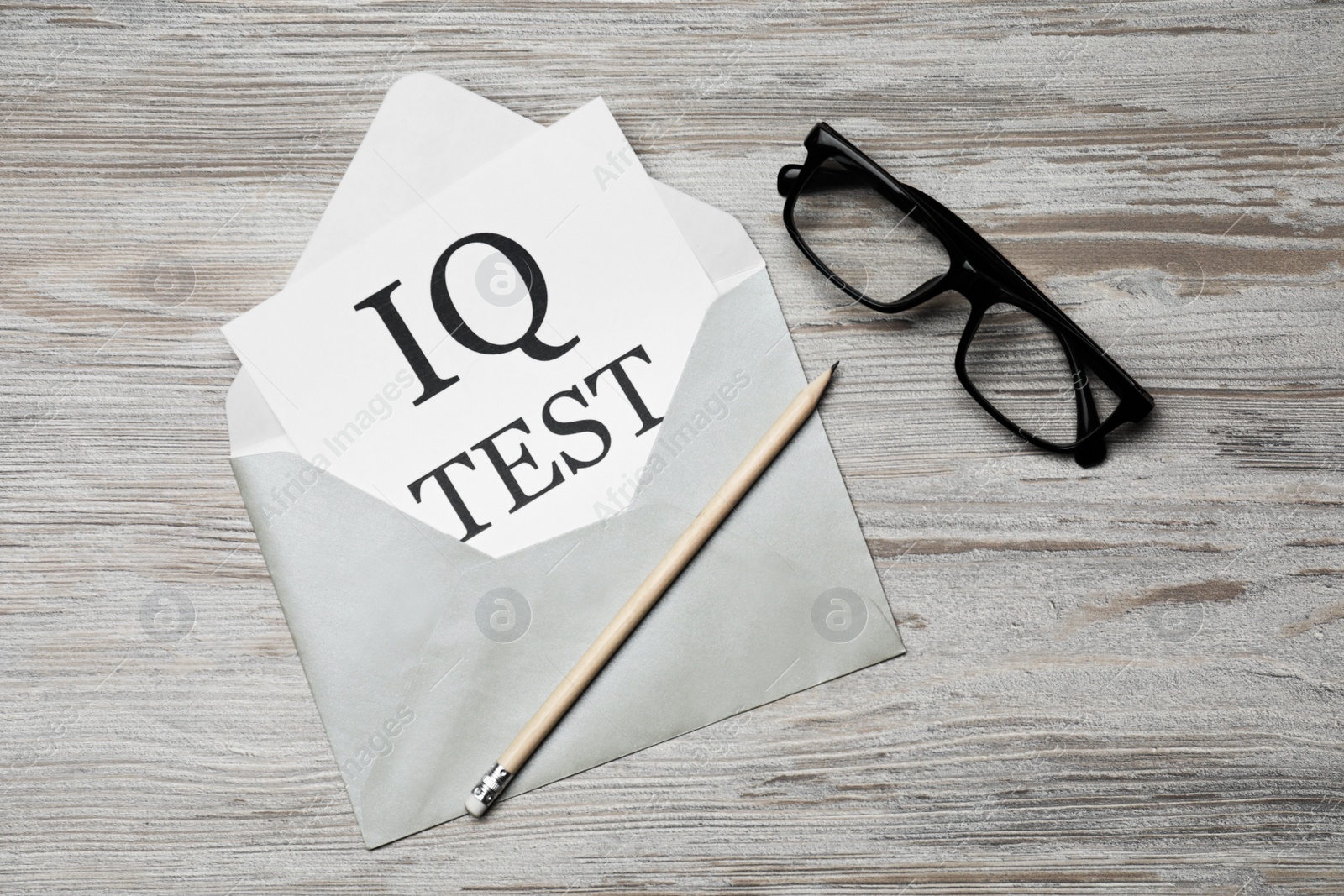 Photo of Paper with words IQ Test in envelope, pencil and glasses on wooden table, flat lay