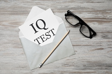 Paper with words IQ Test in envelope, pencil and glasses on wooden table, flat lay
