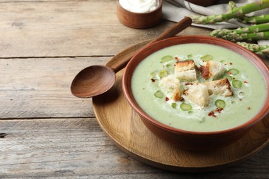 Photo of Delicious asparagus soup with croutons served on wooden table, space for text