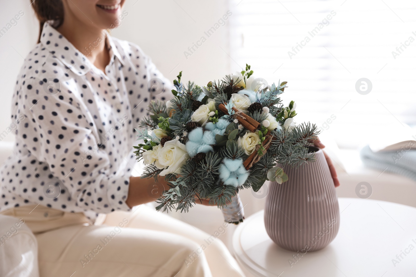 Photo of Woman putting beautiful wedding winter bouquet in vase at home, closeup