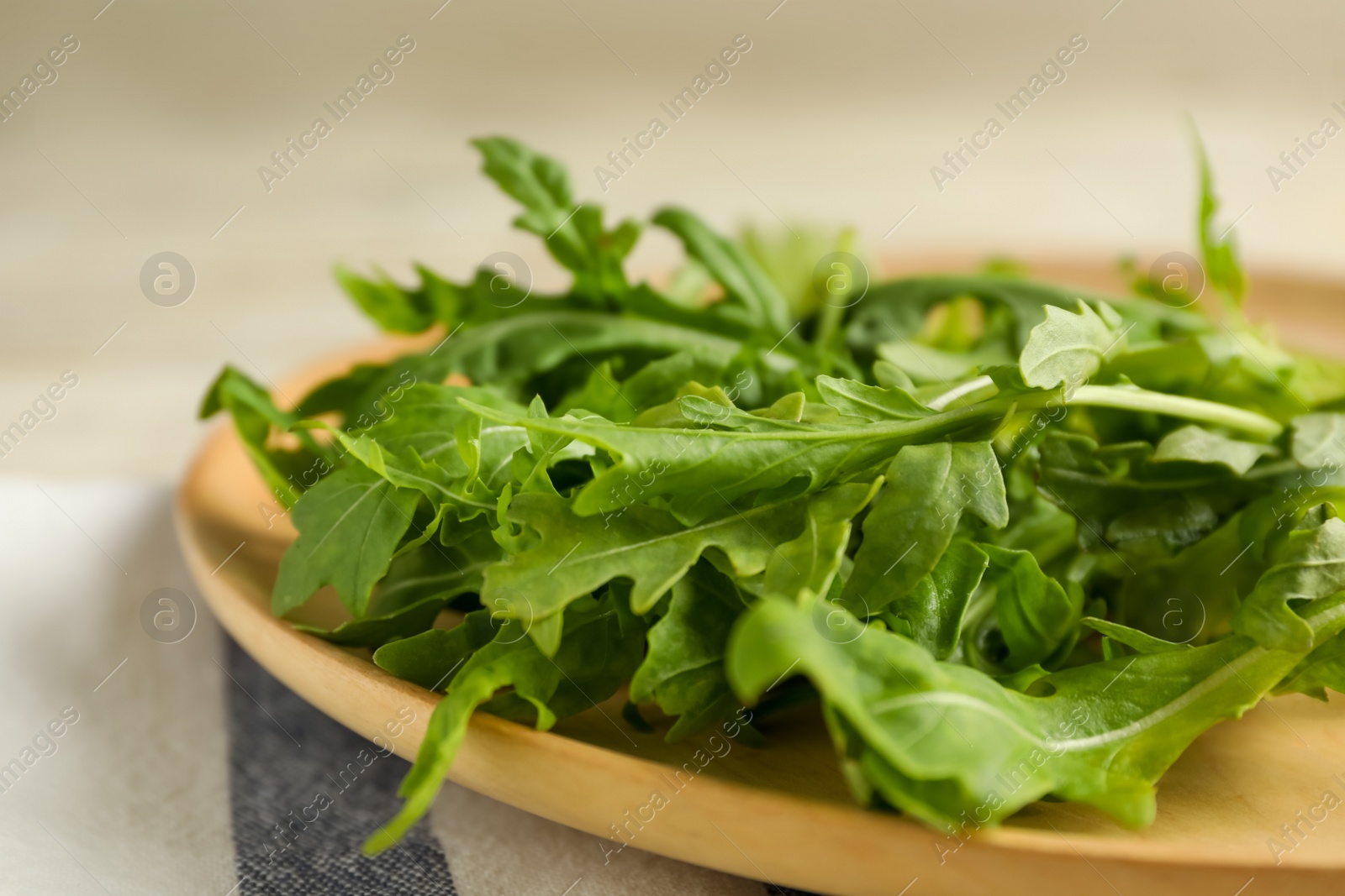 Photo of Fresh arugula leaves on wooden plate, closeup