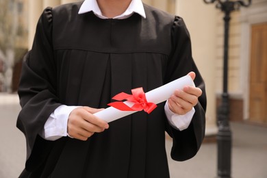 Student with diploma after graduation ceremony outdoors, closeup