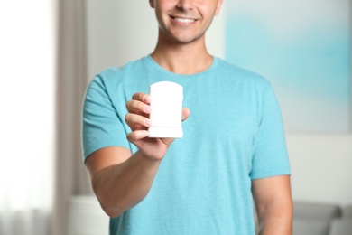 Young man holding deodorant indoors, closeup. Mockup for design