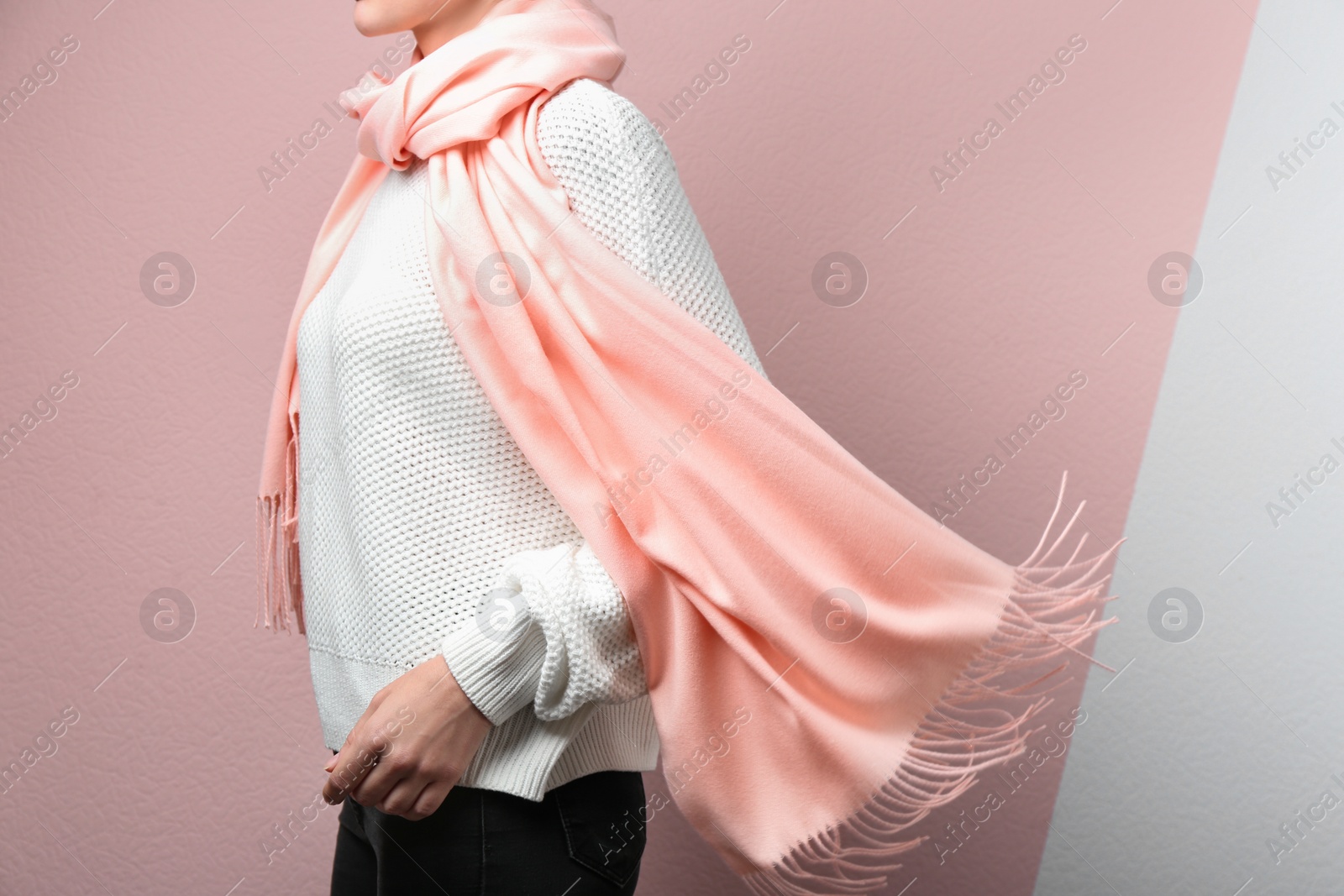 Photo of Woman wearing warm scarf on color background, closeup. Autumn clothes